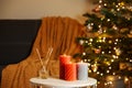 Beautiful candles and reed air freshener near Christmas tree indoors. Cosy atmosphere