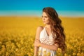 Beautiful carefree girl with long curly healthy hair over Yellow rape field landscape background. Attracive brunette with blowing