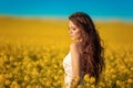 Beautiful carefree girl with long curly healthy hair over Yellow rape field landscape background. Attracive brunette with blowing