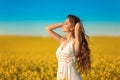 Beautiful carefree girl with long curly healthy hair over Yellow rape field landscape background. Attracive brunette with blowing