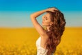 Beautiful carefree girl with long curly healthy hair over Yellow rape field landscape background. Attracive brunette with blowing