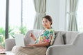 Beautiful carefree woman in casual showing credit card to camera while working with laptop on sofa Royalty Free Stock Photo