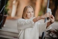 Beautiful casual blonde stylish fashion woman with a phone in her hand make selfie. European buildings and street on a background. Royalty Free Stock Photo