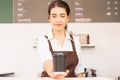 Beautiful caucasian barista woman shows takeaway coffee cup in one hand forward and looking to coffee cup at coffee bar Royalty Free Stock Photo