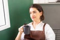 Beautiful caucasian barista woman sits blanky and looks outside window in breaking time while holding hot coffee glasses in coffee Royalty Free Stock Photo