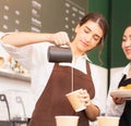 Beautiful caucasian barista women fill white milk into takeaway hot coffee cup at coffee bar in cafe coffee shop Royalty Free Stock Photo