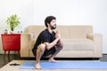 Beautiful caucasian bearded man in black clothes on blue yogamat doing garland pose