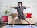 Beautiful caucasian bearded man in black clothes on blue yogamat doing warrior II pose