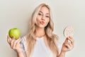 Beautiful caucasian blonde girl holding nachos and healthy green apple looking at the camera blowing a kiss being lovely and sexy Royalty Free Stock Photo