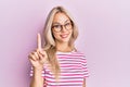 Beautiful caucasian blonde girl wearing casual clothes and glasses smiling with an idea or question pointing finger up with happy Royalty Free Stock Photo