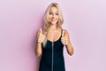 Beautiful caucasian blonde girl wearing sexy party dress success sign doing positive gesture with hand, thumbs up smiling and