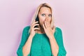 Beautiful caucasian blonde woman having conversation talking on the smartphone covering mouth with hand, shocked and afraid for Royalty Free Stock Photo