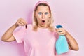 Beautiful caucasian blonde woman holding cockroach and pesticide sprayer afraid and shocked with surprise and amazed expression, Royalty Free Stock Photo