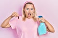 Beautiful caucasian blonde woman holding cockroach and pesticide sprayer celebrating crazy and amazed for success with open eyes
