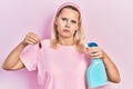 Beautiful caucasian blonde woman holding cockroach and pesticide sprayer relaxed with serious expression on face