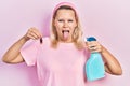 Beautiful caucasian blonde woman holding cockroach and pesticide sprayer sticking tongue out happy with funny expression