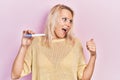 Beautiful caucasian blonde woman holding pregnancy test result pointing thumb up to the side smiling happy with open mouth Royalty Free Stock Photo