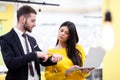 Beautiful Caucasian dark haired girl in yellow posing with businessman wearing suit. Happy colleagues with a laptop in a modern Royalty Free Stock Photo