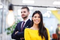 Beautiful Caucasian dark haired girl in yellow posing with businessman wearing suit. Happy colleagues in a modern office