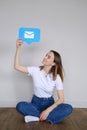 A beautiful caucasian girl sits on the floor and holds a icon messages in messenger above her head