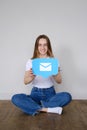 A beautiful caucasian girl sits on the floor and holds a icon messages in messenger in front