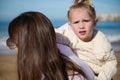 Beautiful child girl looking at camera while her loving mother carrying her on her back, walking together on the beach Royalty Free Stock Photo