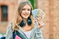 Beautiful caucasian student teenager using headphones holding canadian dollars at the city