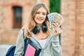 Beautiful caucasian student teenager using headphones holding canadian dollars at the city