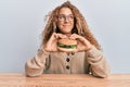 Beautiful caucasian teenager girl eating a tasty classic burger smiling looking to the side and staring away thinking Royalty Free Stock Photo