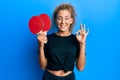 Beautiful caucasian teenager girl holding red ping pong rackets doing ok sign with fingers, smiling friendly gesturing excellent