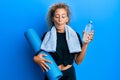 Beautiful caucasian teenager girl holding yoga mat and water bottle making fish face with mouth and squinting eyes, crazy and Royalty Free Stock Photo