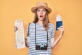 Beautiful caucasian tourist woman holding city map and passport afraid and shocked with surprise and amazed expression, fear and