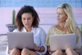 Beautiful caucasian woman and attractive afro latin mixed girl working online together with laptop computer outdoors as digital no Royalty Free Stock Photo