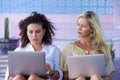Beautiful caucasian woman and attractive afro latin mixed girl working online together with laptop computer outdoors as digital no Royalty Free Stock Photo