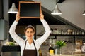 Beautiful Caucasian woman in barista apron holding empty blackboard sign inside coffee shop - ready to insert text Royalty Free Stock Photo