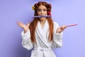 Redhead young girl in hair curlers isolated in purple background Royalty Free Stock Photo