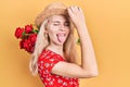 Beautiful caucasian woman with blond hair holding bouquet of red roses sticking tongue out happy with funny expression