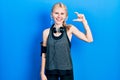 Beautiful caucasian woman with blond hair wearing sportswear smiling and confident gesturing with hand doing small size sign with Royalty Free Stock Photo