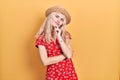 Beautiful caucasian woman with blond hair wearing summer hat looking confident at the camera with smile with crossed arms and hand Royalty Free Stock Photo