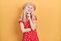 Beautiful caucasian woman with blond hair wearing summer hat looking confident at the camera smiling with crossed arms and hand Royalty Free Stock Photo