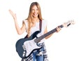 Beautiful caucasian woman with blonde hair playing electric guitar celebrating victory with happy smile and winner expression with Royalty Free Stock Photo