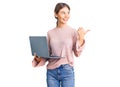 Beautiful caucasian woman with blonde hair working using computer laptop pointing thumb up to the side smiling happy with open Royalty Free Stock Photo