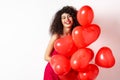 Beautiful caucasian woman with curly hair, wearing date dress, holding romantic red hearts balloons and laughing on Royalty Free Stock Photo