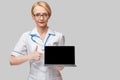 Beautiful Caucasian woman doctor or nurse holding a laptop pc computer with blank screen standing over grey background Royalty Free Stock Photo