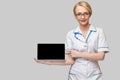 Beautiful Caucasian woman doctor or nurse holding a laptop pc computer with blank screen standing over grey background Royalty Free Stock Photo