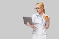 Beautiful Caucasian woman doctor or nurse holding a laptop pc computer and cup of coffee to go standing over grey Royalty Free Stock Photo