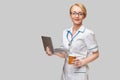 Beautiful Caucasian woman doctor or nurse holding a laptop pc computer and cup of coffee to go standing over grey Royalty Free Stock Photo