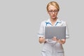 Beautiful Caucasian woman doctor or nurse holding a laptop pc computer standing over grey background Royalty Free Stock Photo