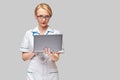 Beautiful Caucasian woman doctor or nurse holding a laptop pc computer standing over grey background Royalty Free Stock Photo