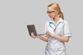 Beautiful Caucasian woman doctor or nurse holding a laptop pc computer standing over grey background Royalty Free Stock Photo